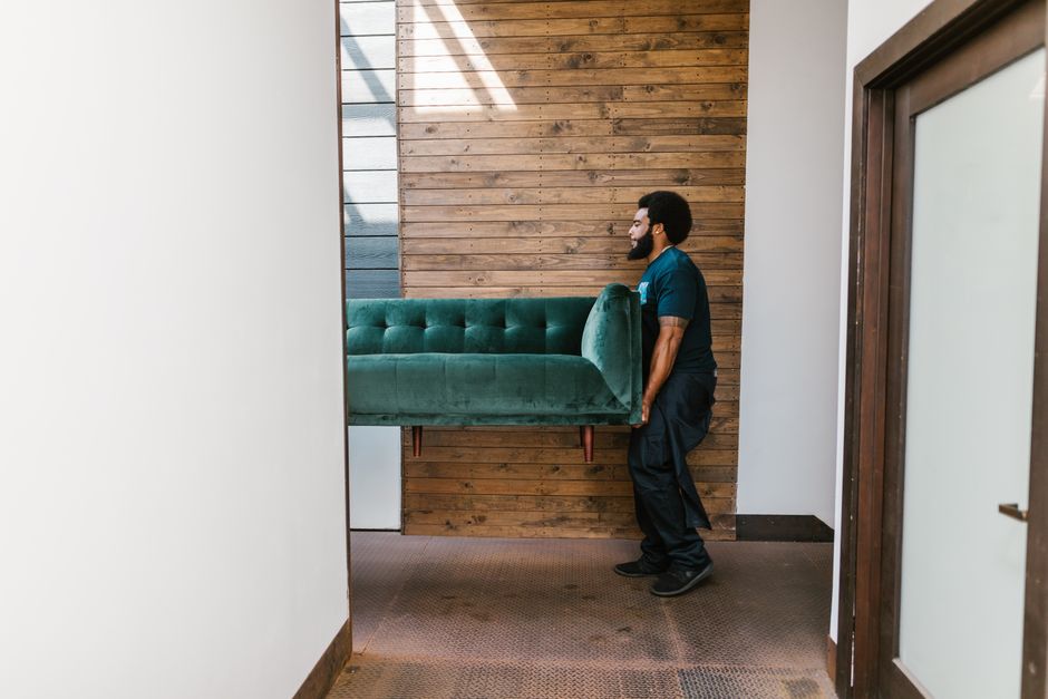 Two movers carefully carrying a heavy sofa out of a living room